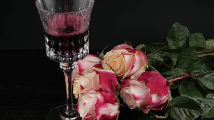 玫瑰花在黑色背景上的水晶酒杯附近