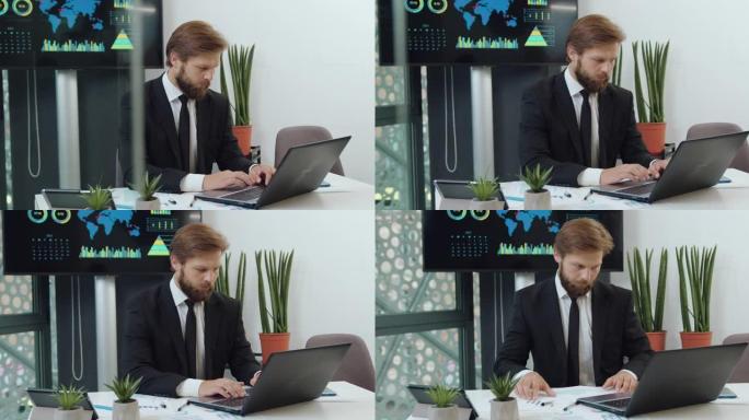英俊、专注、目标明确、留着大胡子、穿着正装的办公室经理肖像，正在比较笔记本电脑数据和财务报告
