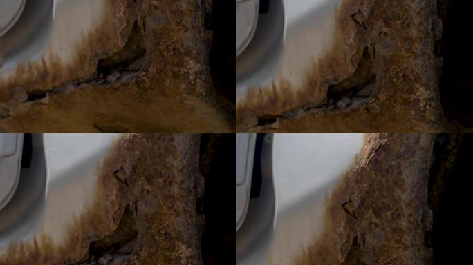 一辆灰色旧车车身上的深锈。旧磨损的油漆金属表面上的锈蚀和腐蚀孔。身体部位修理。需要修理。