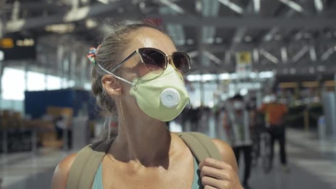 一名头上戴着医用防护口罩的白人女子站在飞机的背景下。冠状病毒sars-cov-2 covid-19。