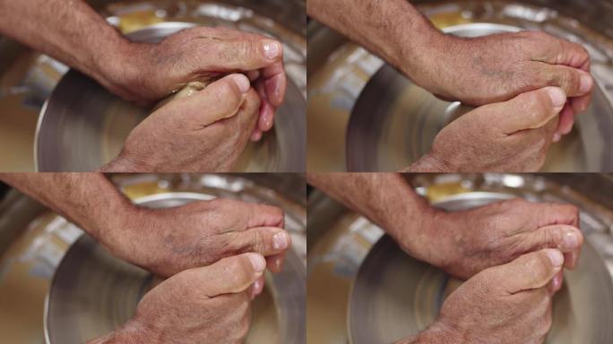 陶艺家的手握着一块在陶艺家轮子上旋转的粘土，使其具有形状，俯视图和特写。男士手在陶工轮上与粘土一起工