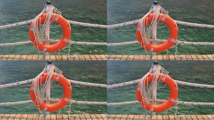 橙色的生命线和海绳在海和蓝天的背景。挂在柱子上的海洋绳索和救生圈。帮助和安全概念
