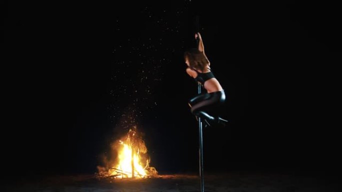 钢管舞。万圣节女巫。身材健美的女体操运动员，穿着黑色皮衣和高跟鞋，在金属旋转杆上进行杂技练习