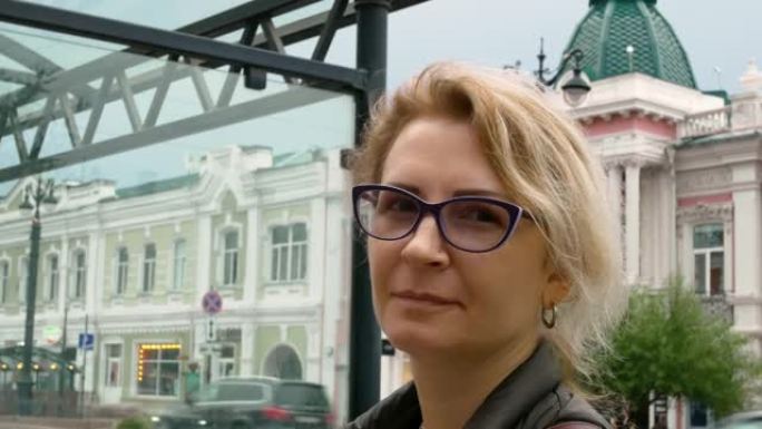 一个戴着眼镜的简单女人站在城市里，汽车在背景中经过，古老的欧洲建筑在站立。城市生活