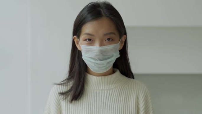 年轻的亚洲妇女戴上病毒和感染疾病的医用防护面膜，看着相机