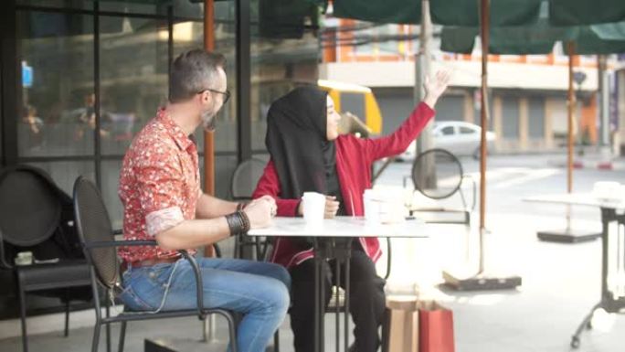 幸福的年轻夫妇在餐桌上聊天和喝咖啡，男人和穆斯林女人是友谊，户外，生活方式观念的朋友。