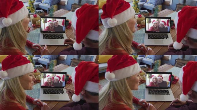 带着圣诞老人帽子微笑的高加索夫妇使用笔记本电脑进行圣诞视频通话屏幕上的夫妇