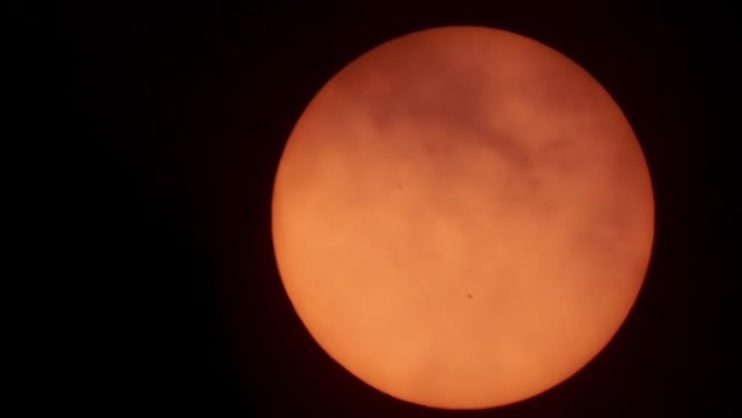 日出时云层后面的望远镜里有太阳黑子的太阳。日落时分，太阳斑透过云层闪耀。太阳耀斑。磁暴，晴风全球变暖
