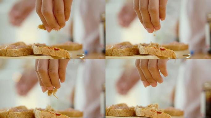 用手将干猪肉丝撒在桌子上的自制三明治上，慢动作。