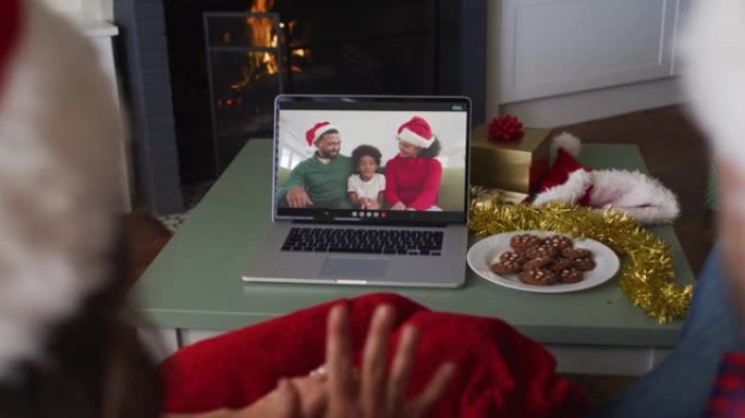 圣诞节期间戴着圣诞老人帽子的高加索夫妇的后视图在笔记本电脑上观看视频