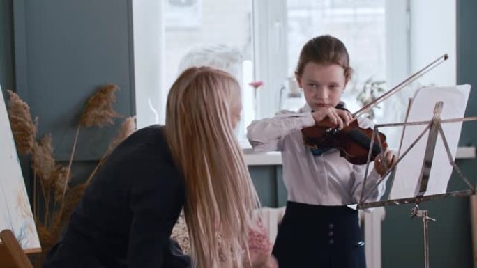 年轻的金发女老师教小女孩如何在拉小提琴时正确握弓