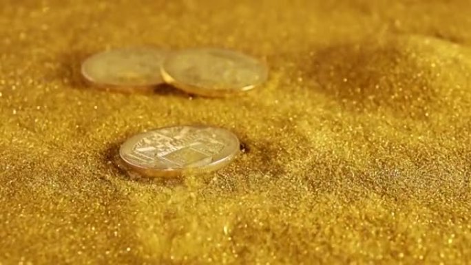 一个比特币落在一张有金色沙子的桌子上。慢动作
