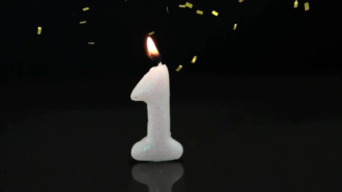 金色五彩纸屑落在黑色背景下的第一个生日燃烧蜡烛上