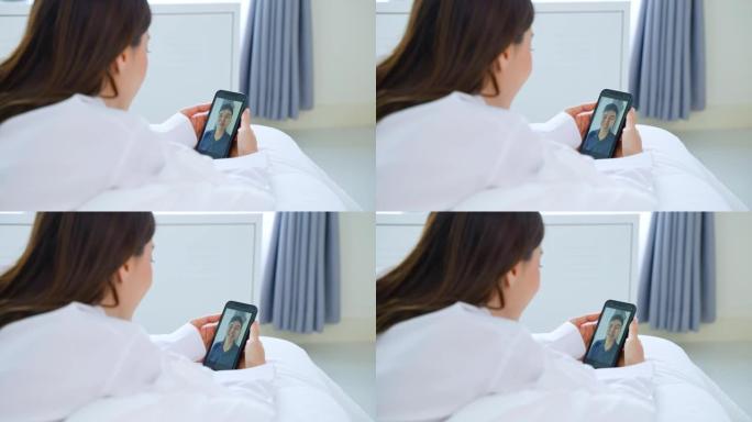 亚洲美女在家床上和男朋友视频通话。穿着睡衣的迷人女孩早上在卧室醒来后，喜欢在手机上的虚拟遥控器上与年