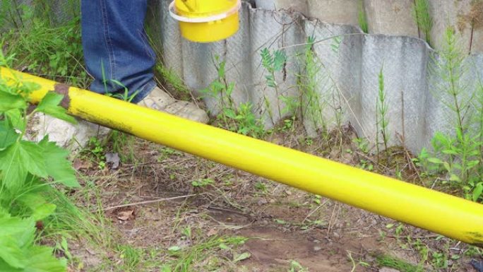 一只手用画笔将生锈的管子涂成黄色。