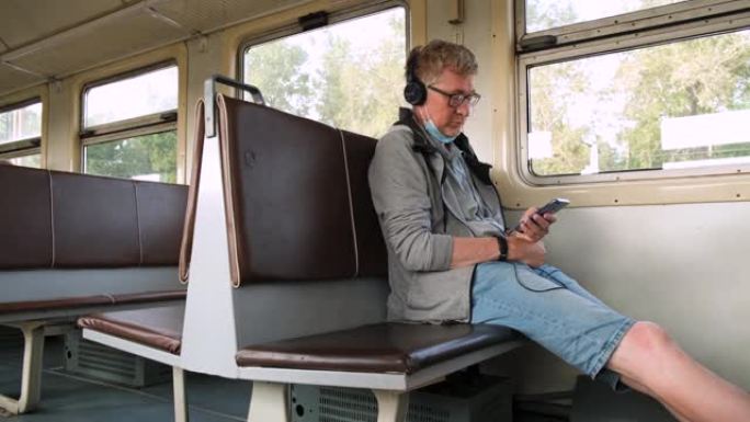 中年男子正戴着耳机和使用电话坐在公共交通工具上。