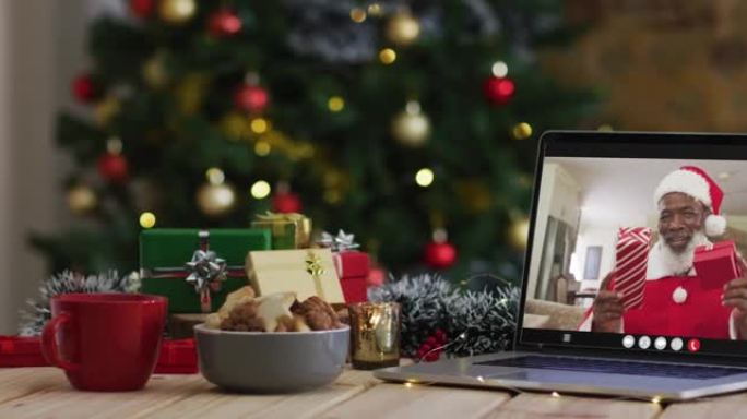 穿着圣诞老人服装的非裔美国人高级男子在笔记本电脑上进行视频通话，并带有圣诞树