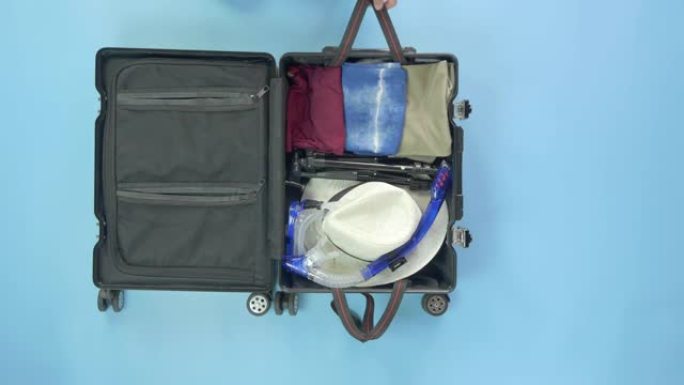 亚洲妇女小心地将笔记本电脑装在手提箱中，以便从蓝色背景的度假屋中进行夏季工作。夏季工作旅行准备概念，