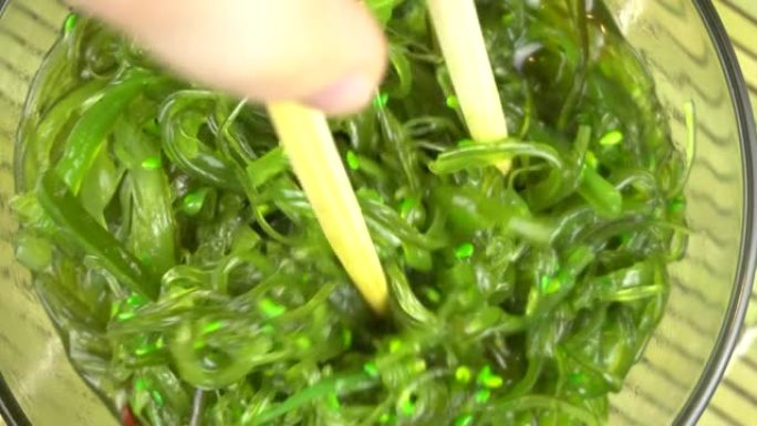 Chuka海藻是由女人的手用筷子举起的。玻璃碗中的Chuka海藻站立。