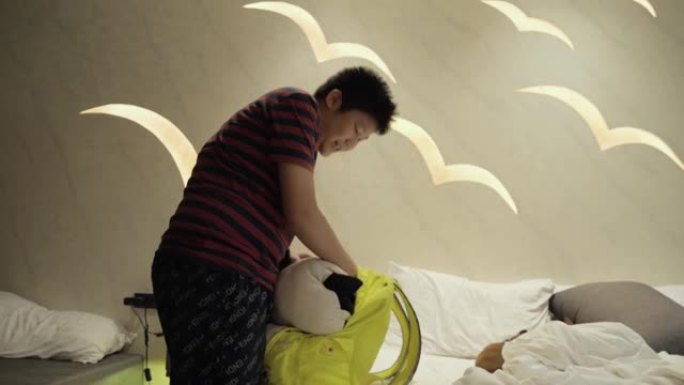亚洲男孩将衣服装在背包和行李中，从酒店出发，生活方式概念。