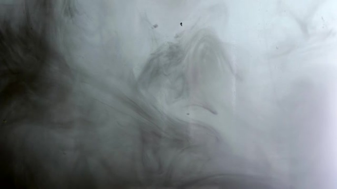 黑色和灰色墨水在水中。油漆掉落，在黑色上形成抽象的云层和变形。慢动作。