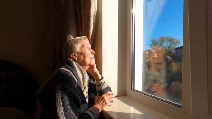 老孤独的幸福女人坐在他家窗户附近