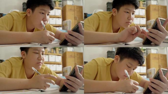 亚洲男孩躺在地板上做作业，同时在家学习在线课程，社交疏远的生活方式理念。