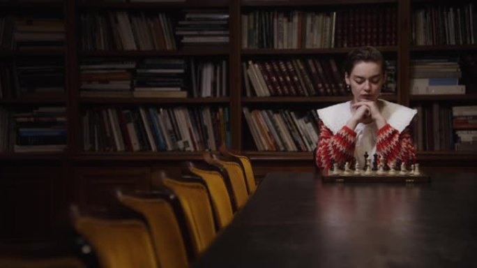 一名年轻女子独自下棋，坐在图书馆的长桌旁