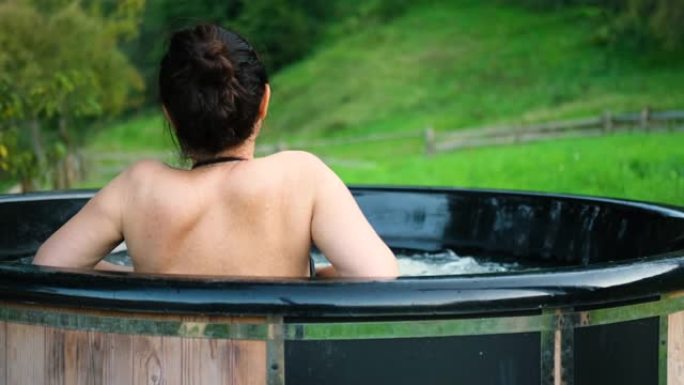 年轻女子在露天浴池里，可以看到山景。