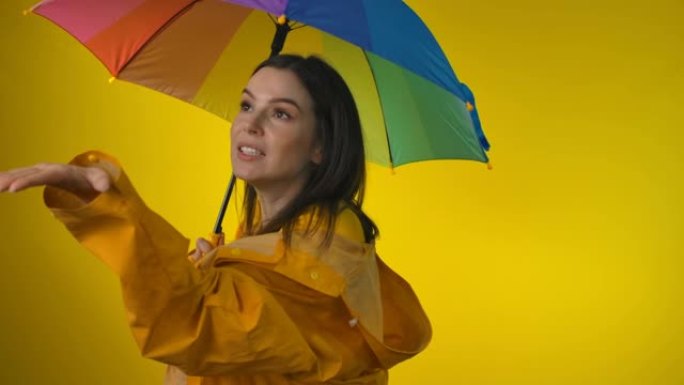 一名身穿黄色雨衣的女子打着彩虹伞正在检查雨水