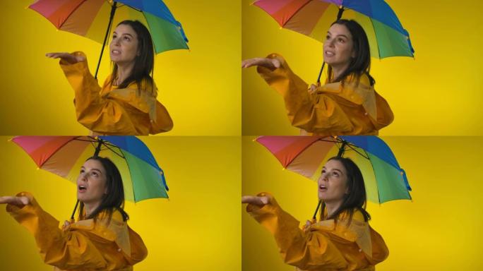 一名身穿黄色雨衣的女子打着彩虹伞正在检查雨水