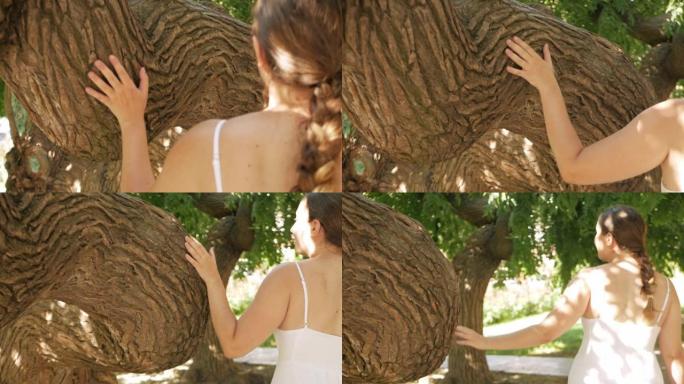 一个城市的游客，一个穿着白色连衣裙的女人抚摸着一棵美丽的树，一个公园。慢动作，与自然的统一，镜头。