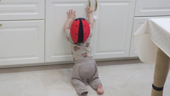 为房屋打气，婴儿戴着安全帽探索厨房橱柜，好奇的小孩试图打开装有儿童安全锁的橱柜门。