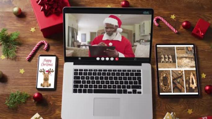 高级非洲裔美国圣诞老人在笔记本电脑上进行视频通话，配有智能手机、平板电脑和装饰品