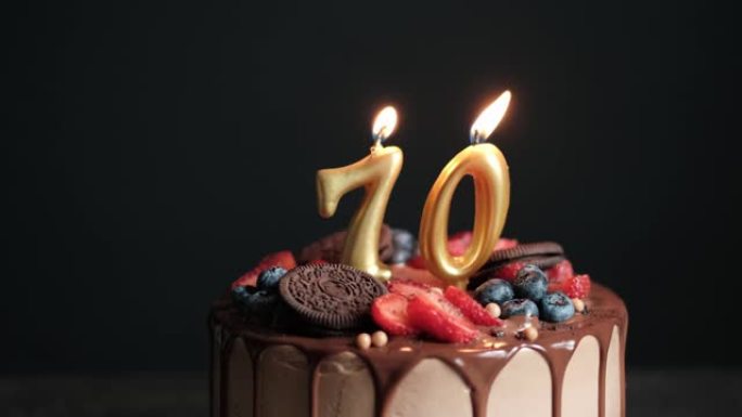 黑色背景上的巧克力生日蛋糕，70号金色蜡烛。70周年生日蛋糕。慢动作