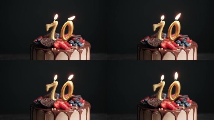 黑色背景上的巧克力生日蛋糕，70号金色蜡烛。70周年生日蛋糕。慢动作