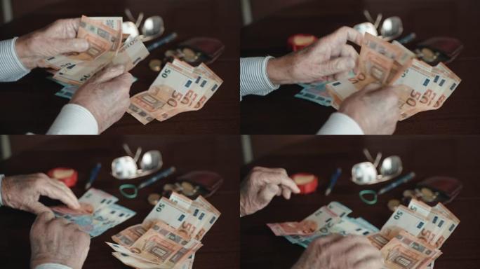 老年男性养老金领取者坐在桌子旁，拿着一叠纸币，数着50欧元的钞票。老人计算自己每月微薄的养老金支付，