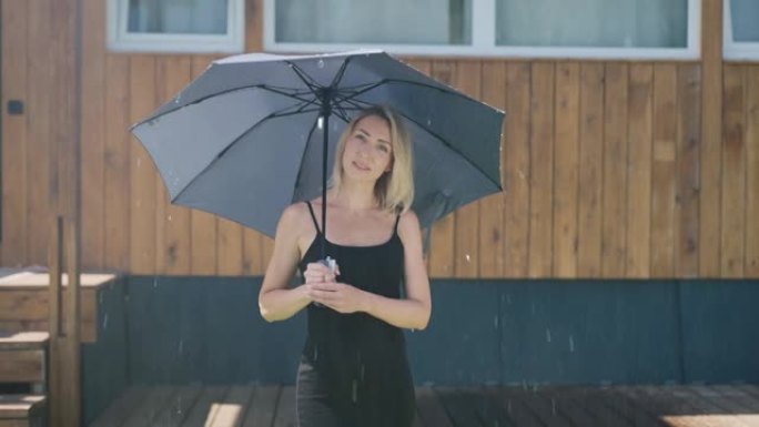 夏日雨中迷人的金发女郎。一个漂亮的女人用雨伞保护自己免受暴雨的袭击