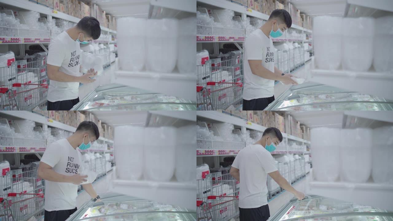 一名年轻的亚洲男子打开玻璃滑门，在超市的冰柜里拿走一包冷冻食品，买一送一促销，省钱，食品行业的技术，