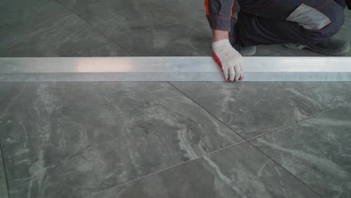 建筑商检查铺设在浴室地板上的瓷砖的表面水平。工人用电线检查地板上瓷砖的高度