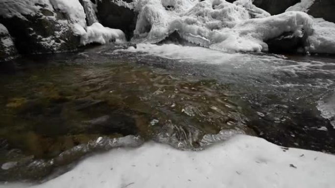 在针叶林中流淌的山区河流的死水特写。冰雪中的冰冻石头。横向移动滑动。广角