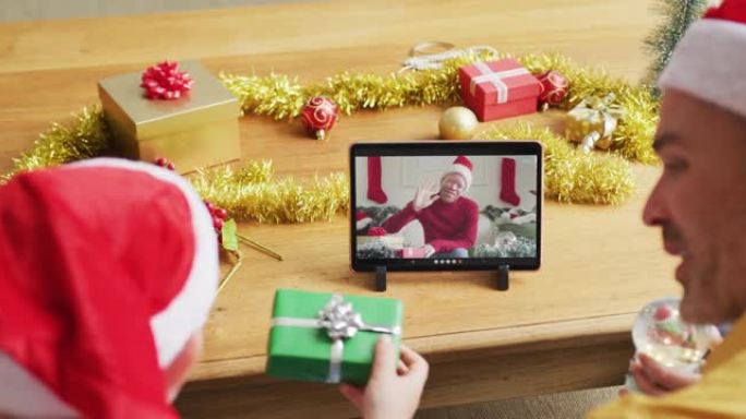 白人父亲和儿子戴着圣诞老人的帽子，使用平板电脑与屏幕上的男人进行圣诞节视频通话