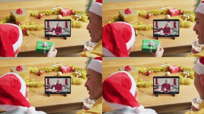 白人父亲和儿子戴着圣诞老人的帽子，使用平板电脑与屏幕上的男人进行圣诞节视频通话