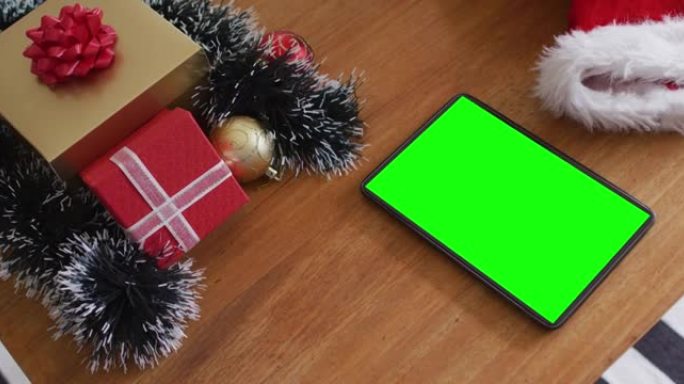 桌子上有绿屏的平板电脑，上面戴着圣诞老人的帽子和圣诞礼物