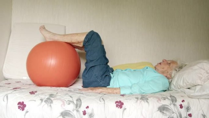 老年白人妇女躺在床上，用健身球进行日常锻炼，以保持健康，灵活和强壮