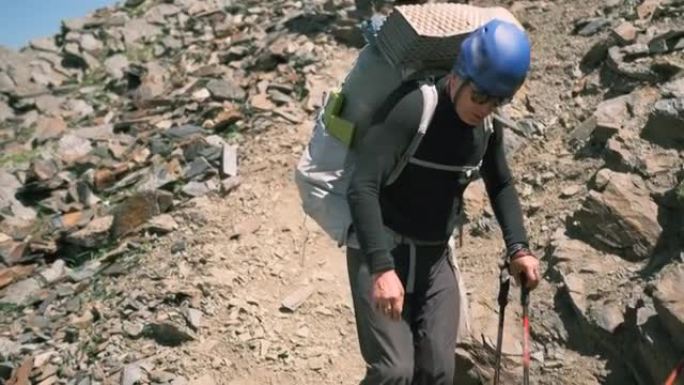 在山上下降时，一名登山者拿着一个大背包走近绳子，抓住了它。