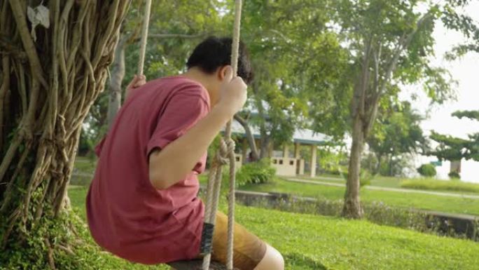 亚洲男孩坐在户外公园树下悬挂的长袍秋千上，生活方式理念。