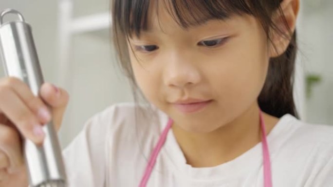 快乐的亚洲孩子在家里学习做饼干，女孩在搅拌碗里搅拌面粉。