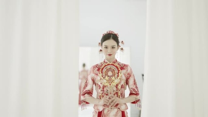 年轻的中国妇女穿着传统的嫁衣，红色的秀和衣服，拿着传统的中国粉丝，对着镜头微笑，以慢动作拍摄