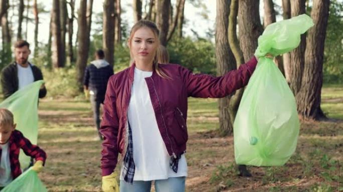 与志同道合的志愿者一起在公园里收集垃圾时站在镜头前的漂亮严肃的活跃女孩的特写镜头